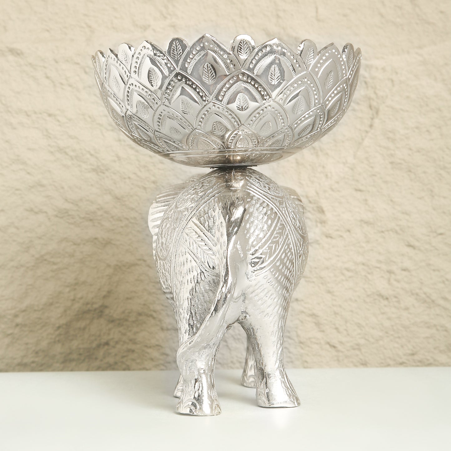 Decorative silver bowl on an elephant stand with a textured beige background