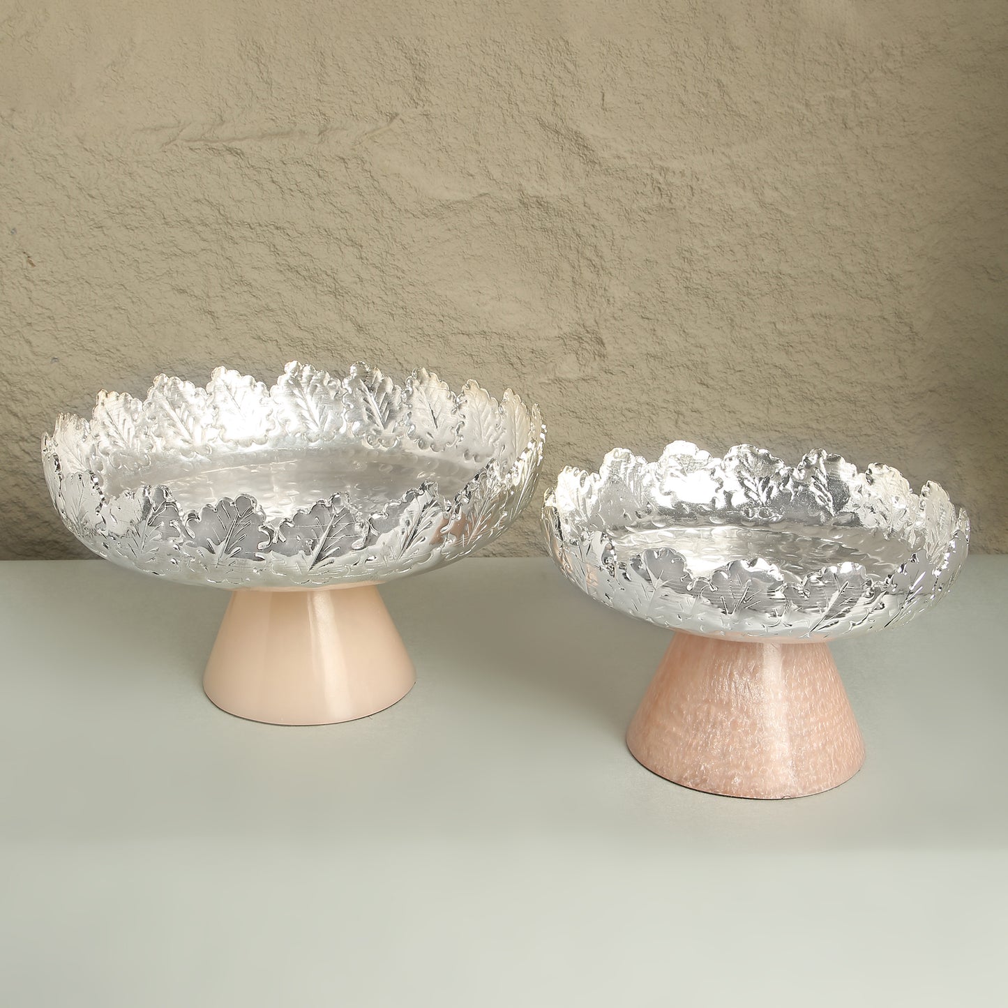 Two decorative glass bowls with textured surfaces on pink stands against a neutral background