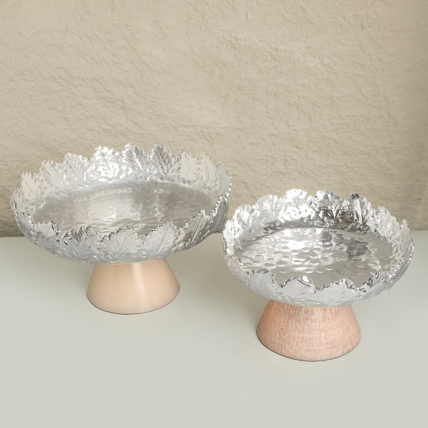 Two glass bowls with textured surfaces on wooden stands against a beige background