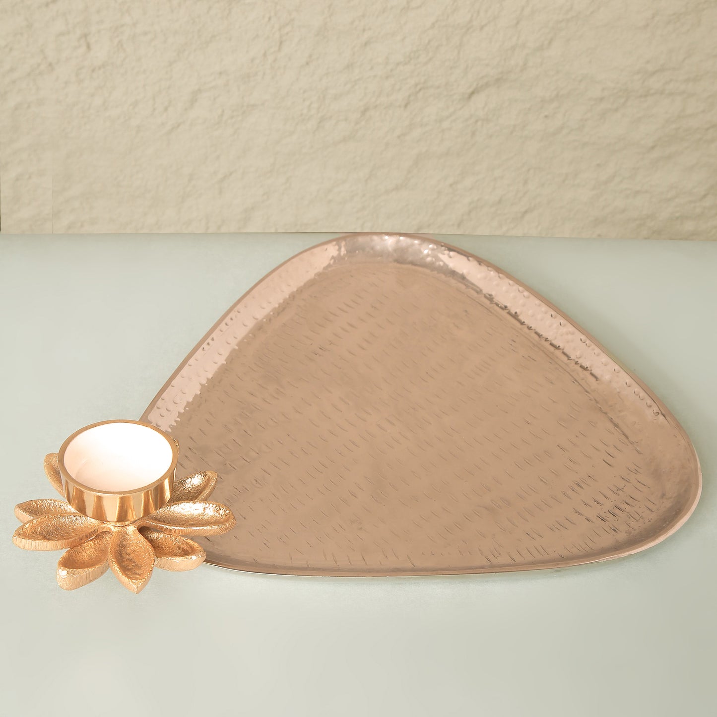 Triangular copper tray with floral design on a light green surface