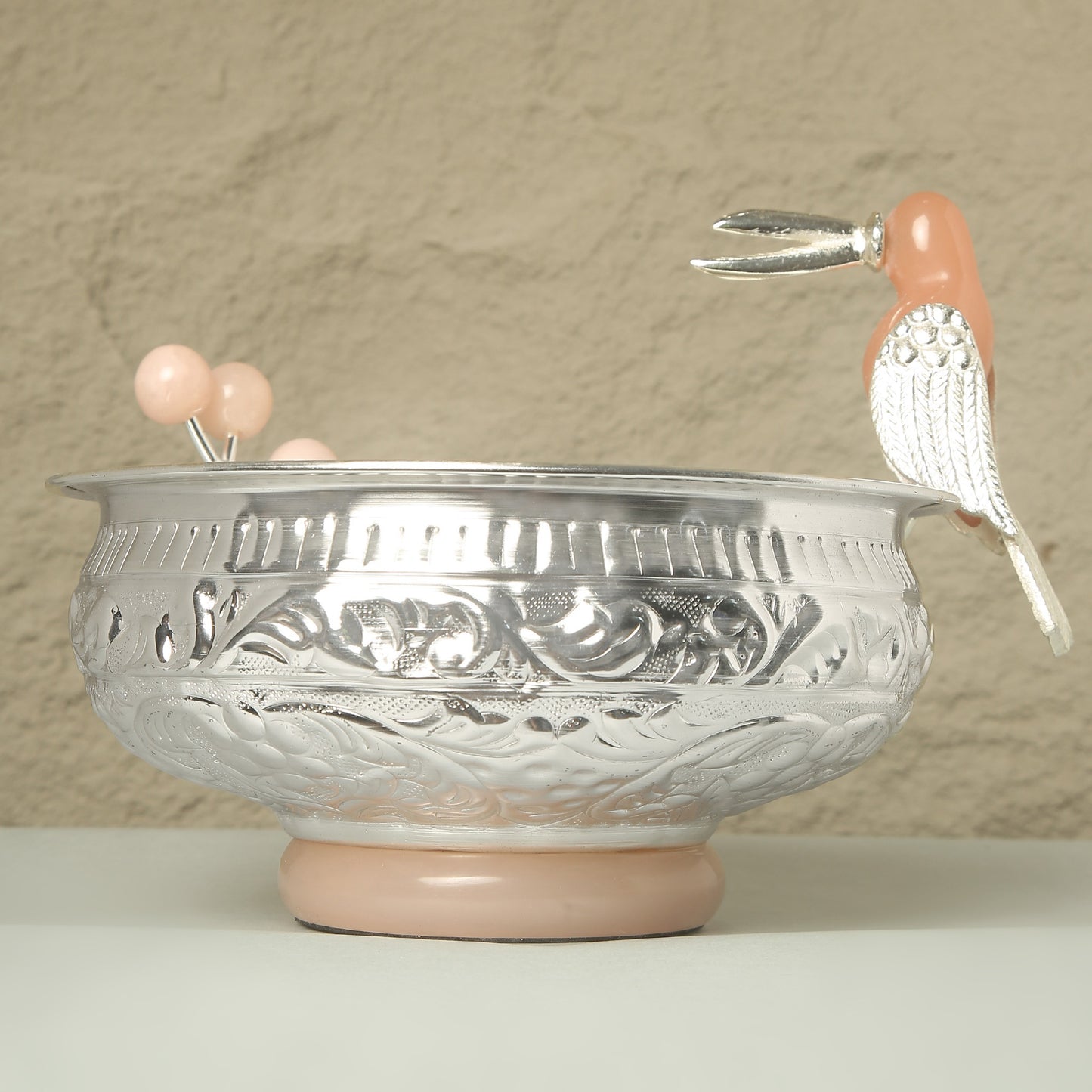 Decorative silver bowl with pink base and handles on a beige background