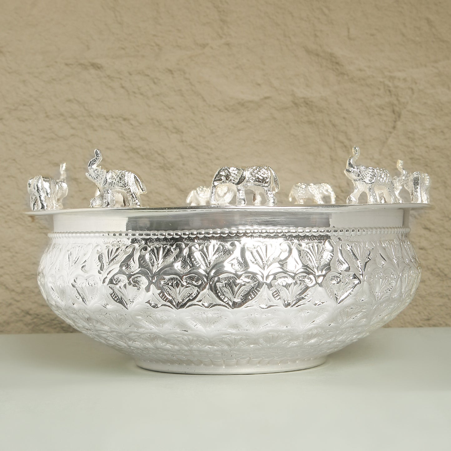 Decorative silver bowl with intricate patterns and small elephant figurines on a beige background