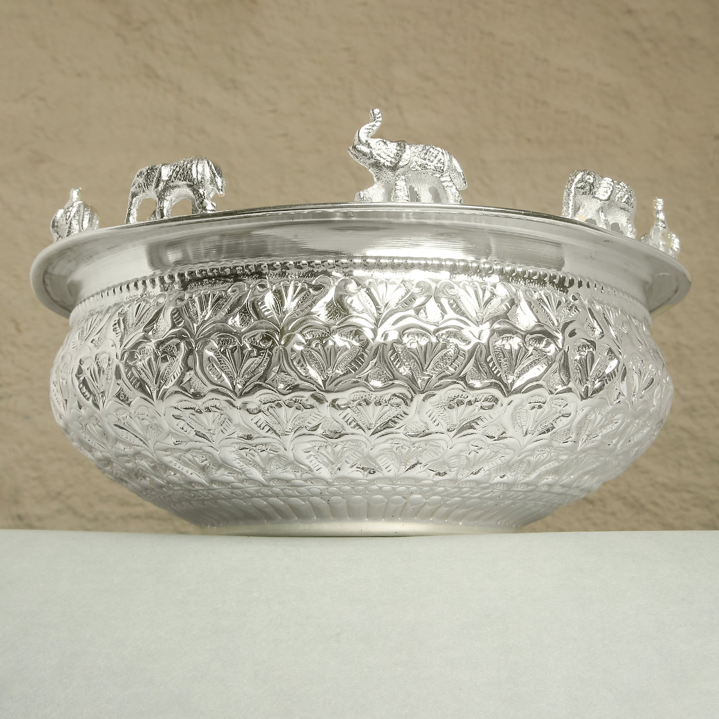 Decorative silver bowl with intricate patterns and small figurines on a beige background