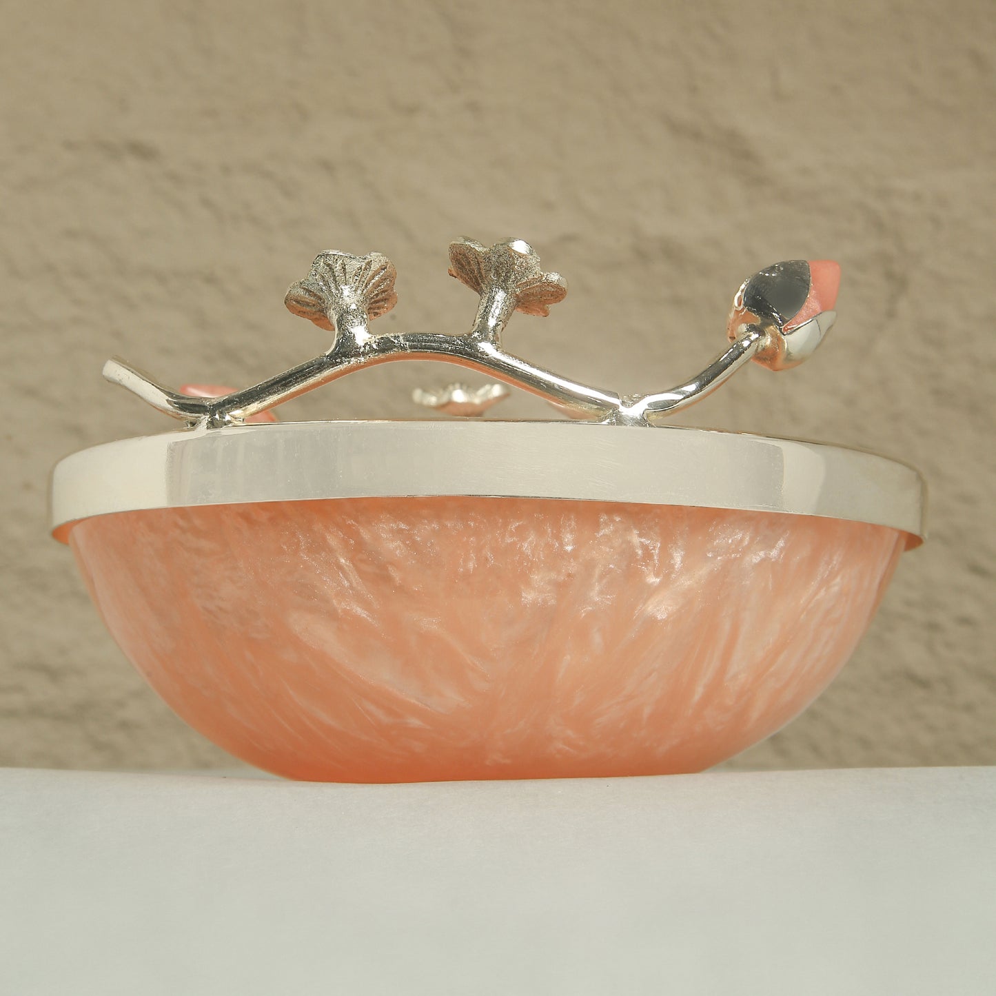 Decorative bowl with silver rim and coral-colored interior on a neutral background