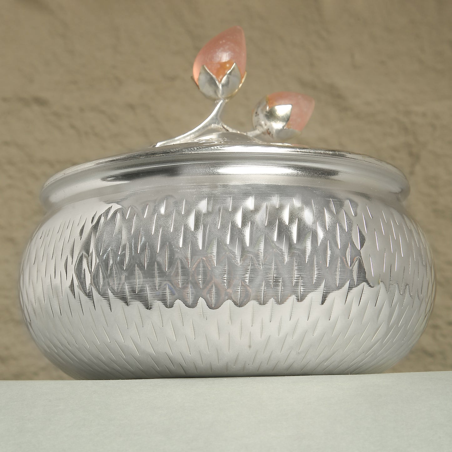 Silver textured container with a decorative lid on a beige background