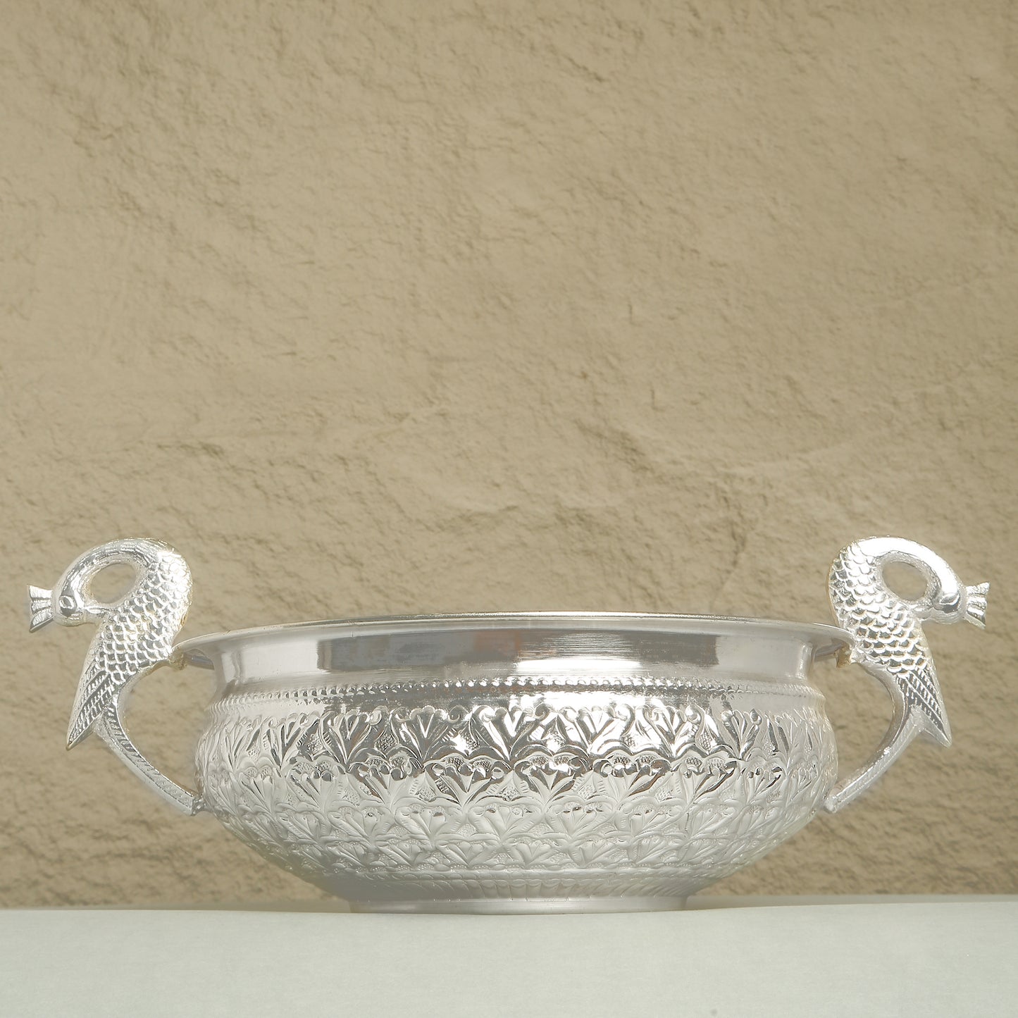 Silver bowl with decorative handles on a beige background