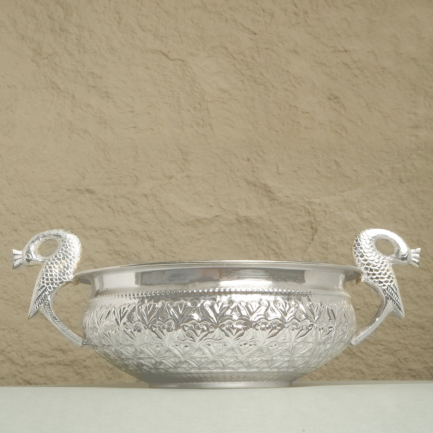 Silver bowl with decorative handles on a beige background