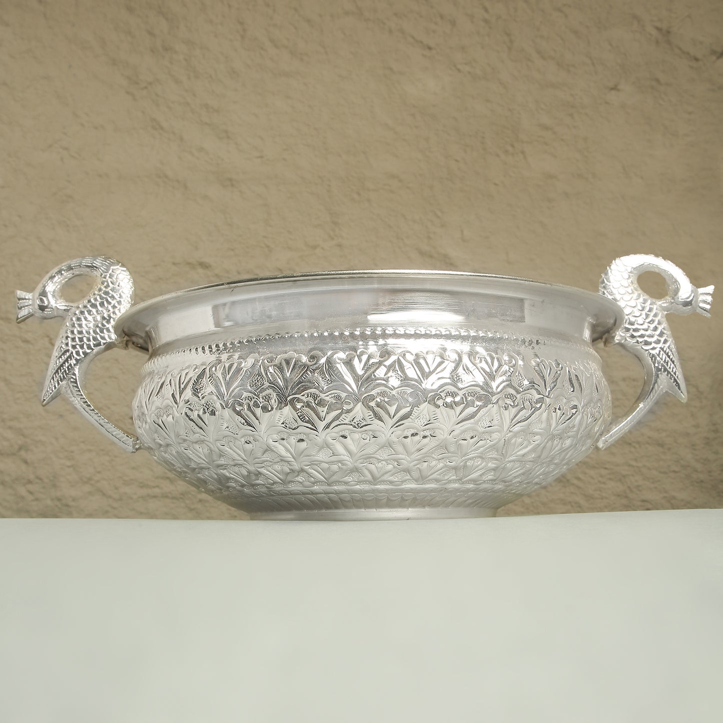 Decorative silver bowl with handles on a beige background