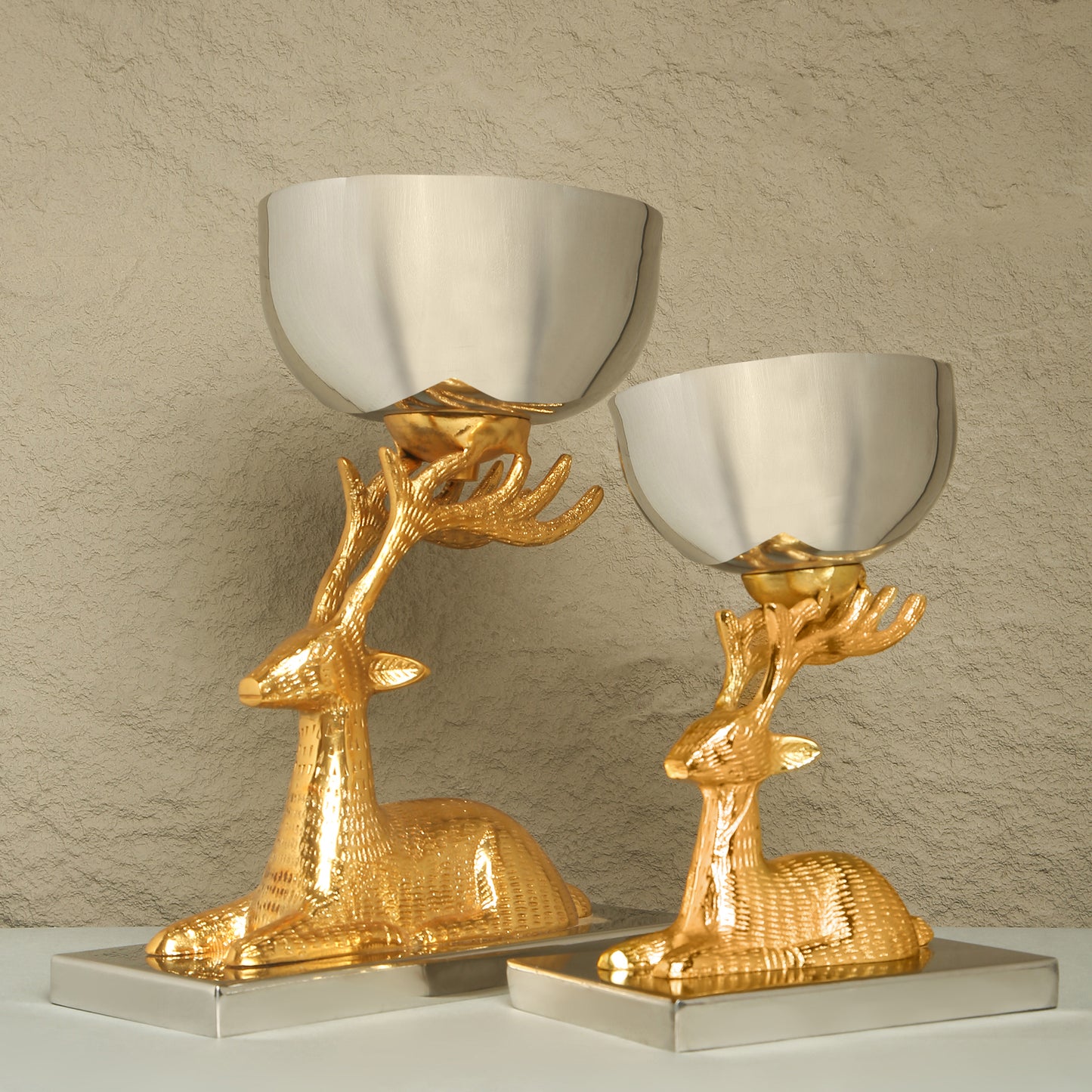 Two gold deer-shaped candle holders with silver bowls on a neutral background