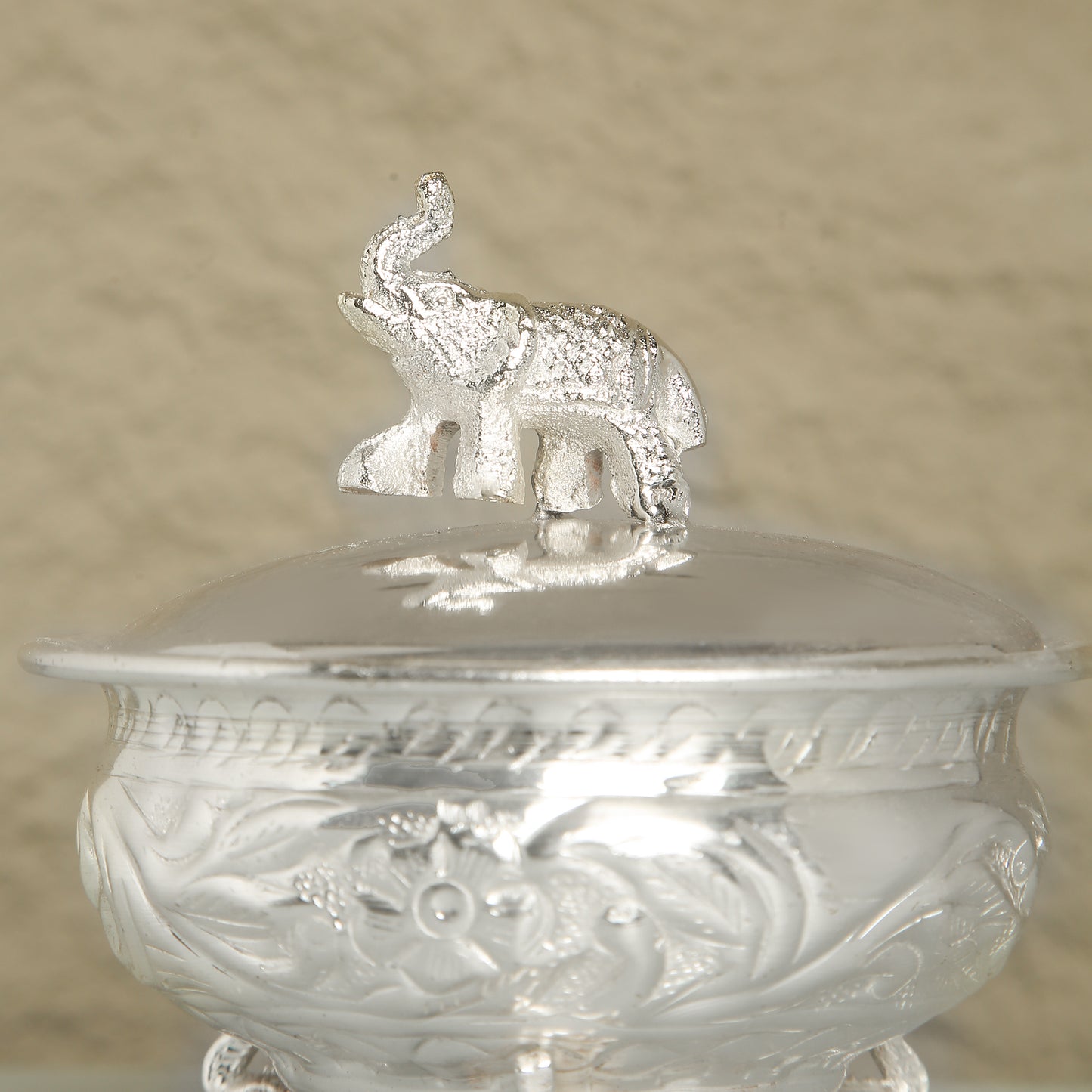 Silver container with an elephant on top against a beige background