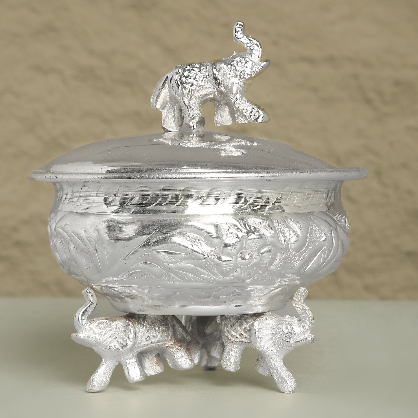 Silver decorative container with elephant design on a beige background