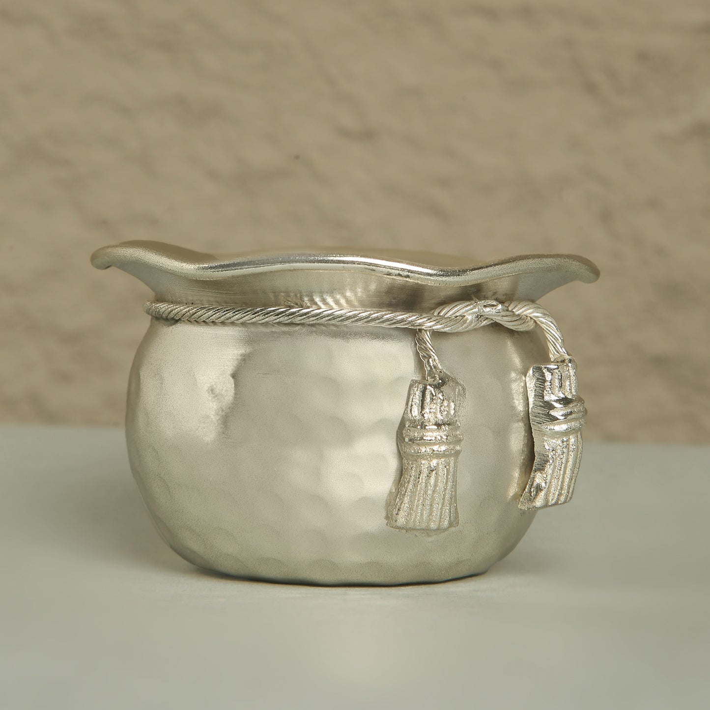 Silver decorative bowl with tassels on a neutral background