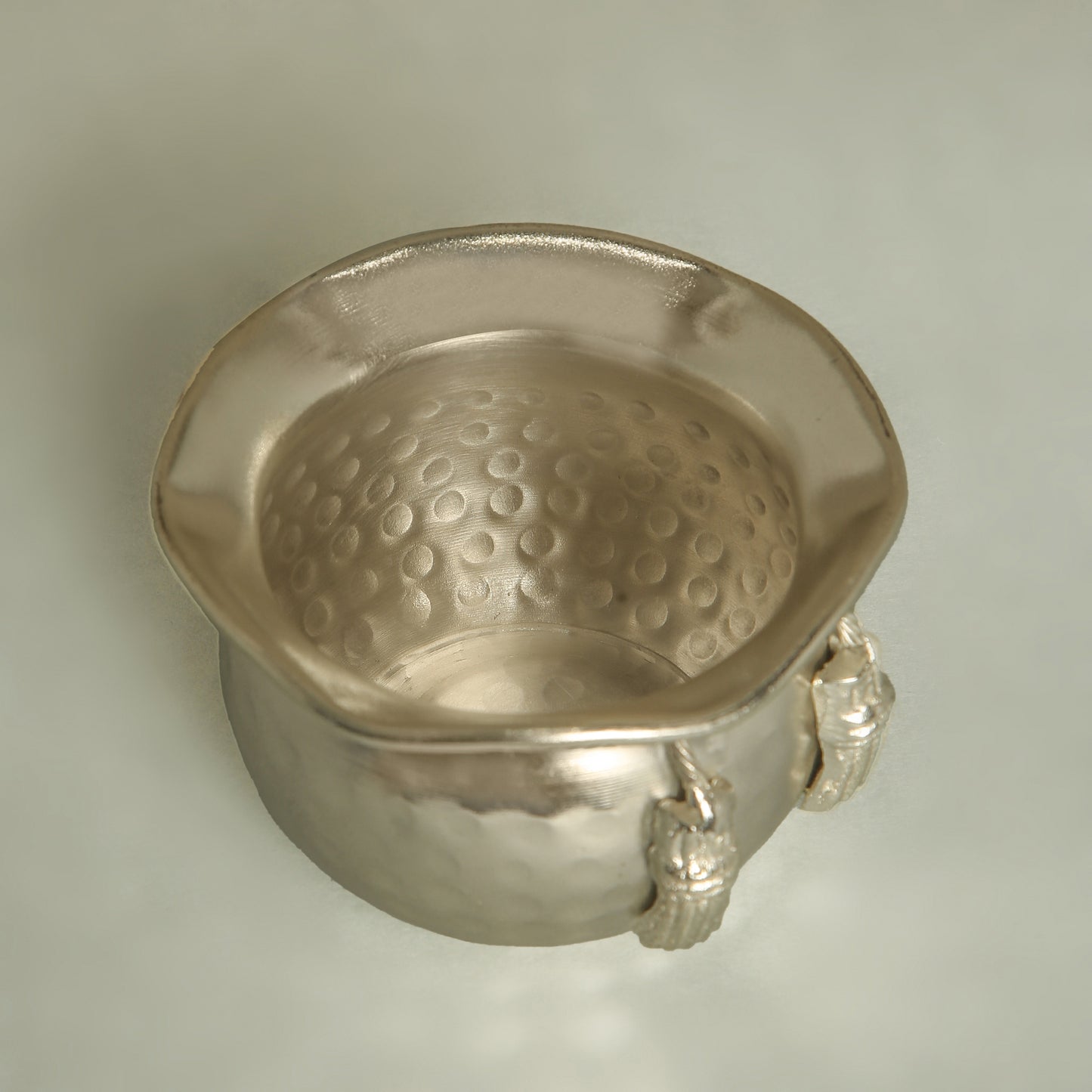 Silver bowl with textured interior and lion head handles on a light gray background