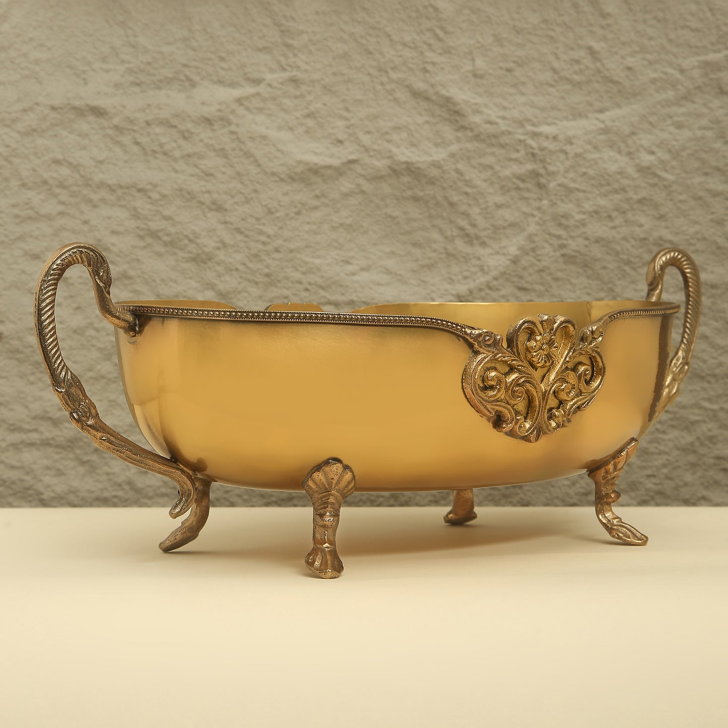 Decorative yellow bowl with ornate gold handles and base on a beige surface.