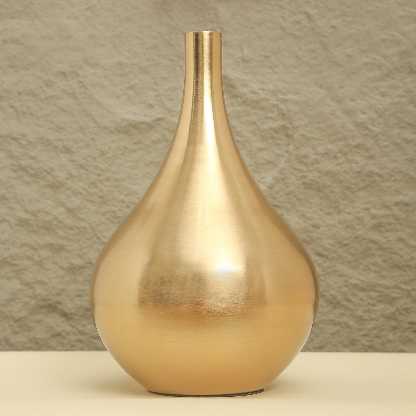 Gold vase on a beige surface with a textured brown wall background