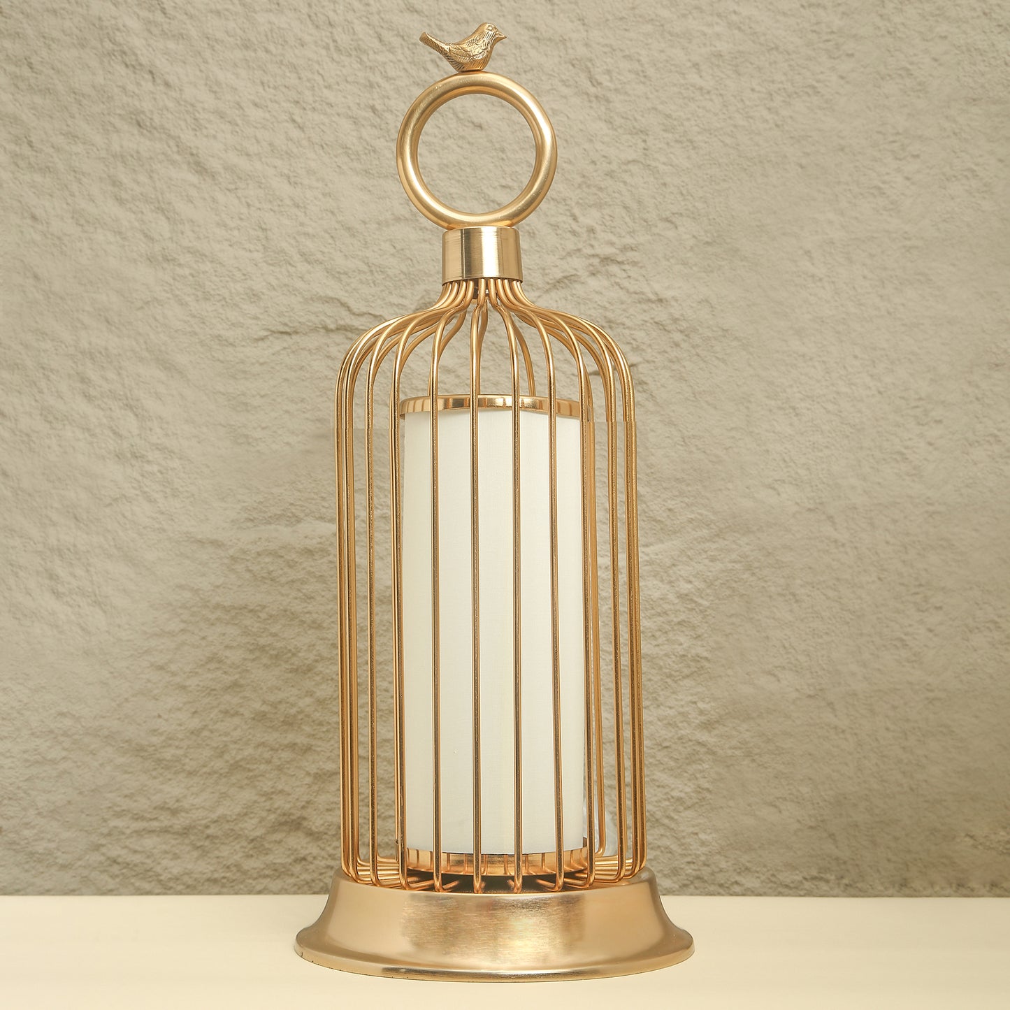 Gold birdcage-shaped lantern with a white candle on a beige background