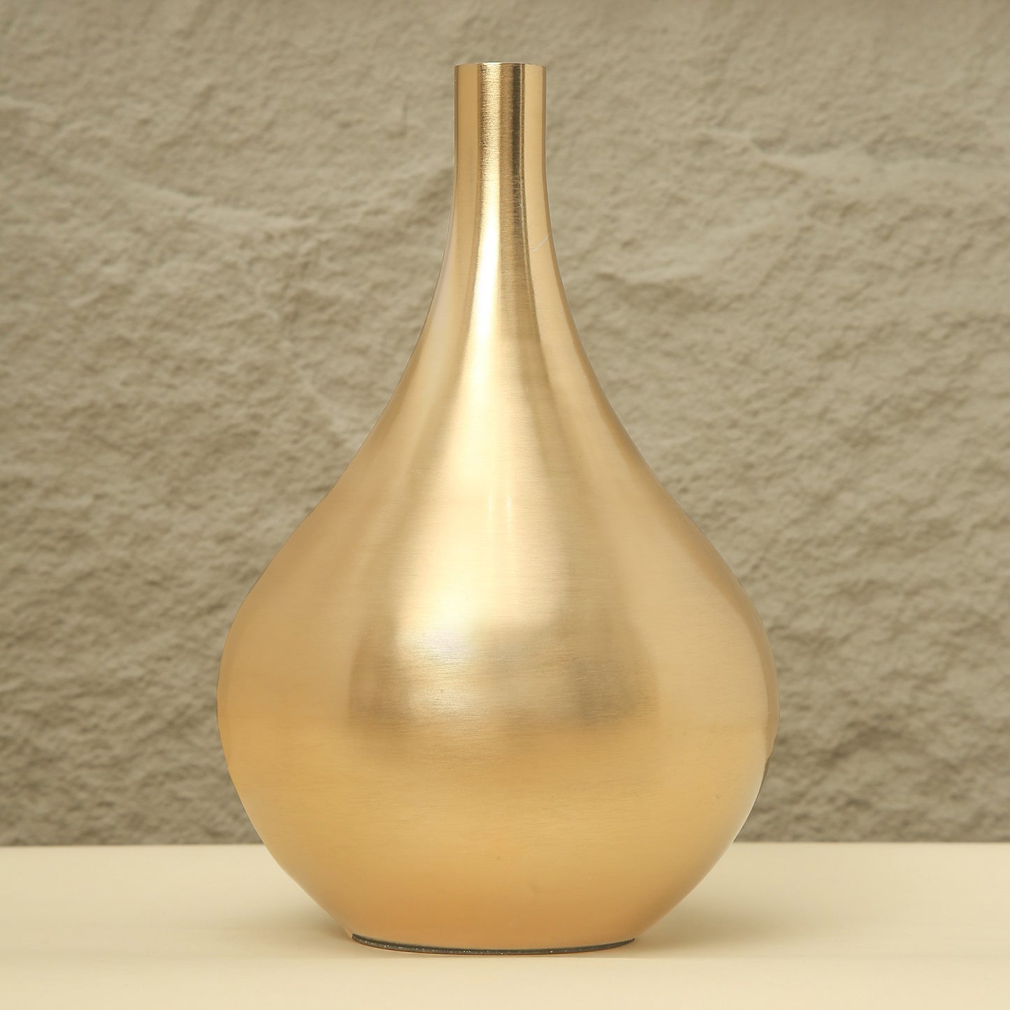 Gold vase on a beige surface with a textured brown wall background