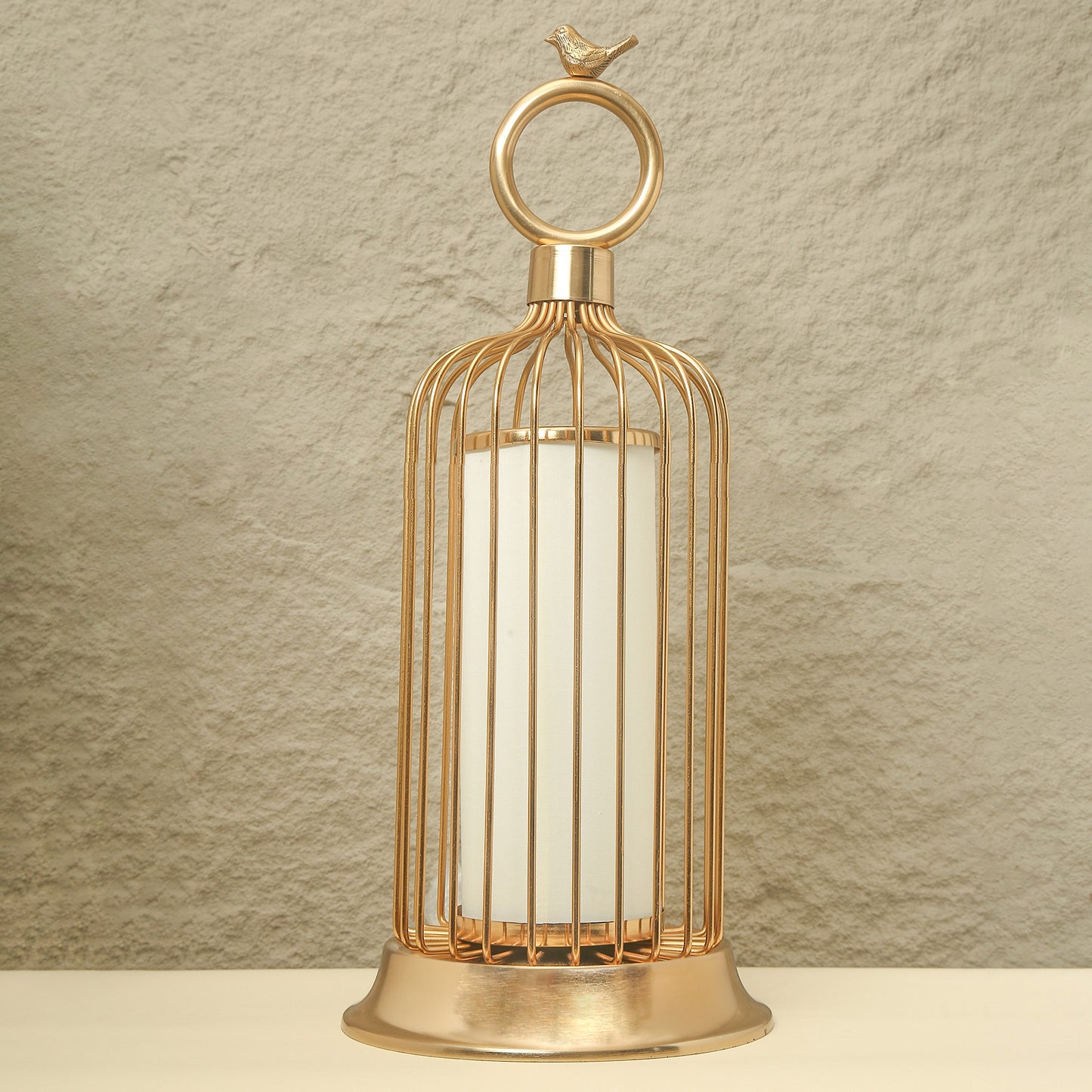 Gold birdcage lantern with a white candle on a beige background