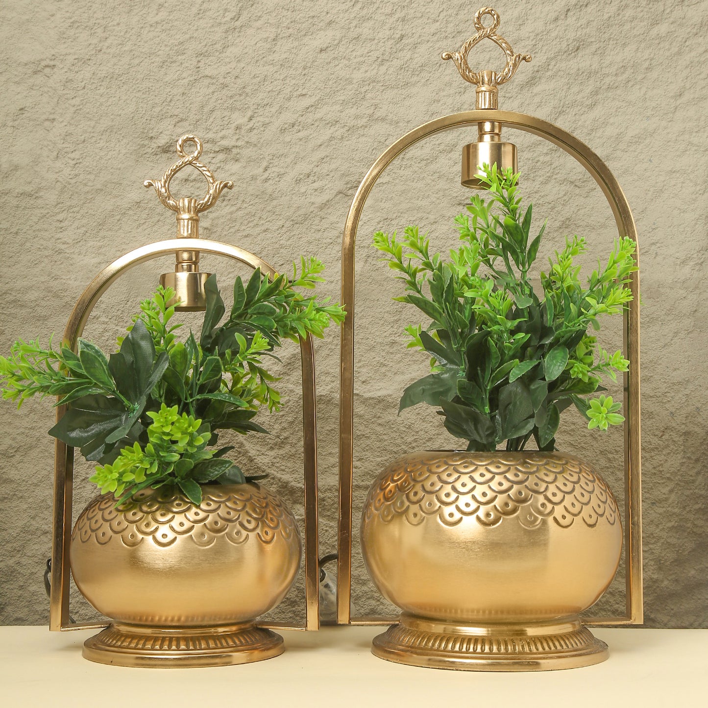 Two gold decorative vases with planters on a neutral background