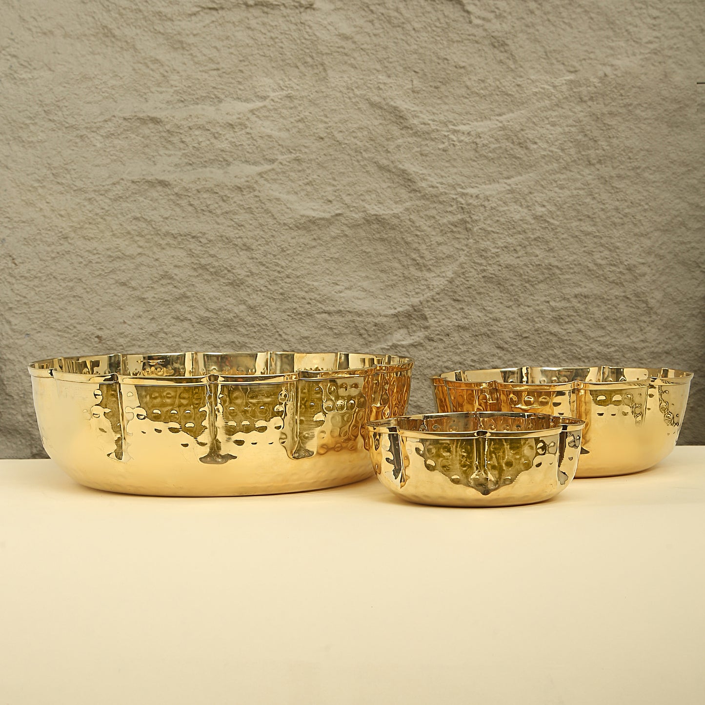 Set of gold bowls on a beige surface with a textured gray wall background