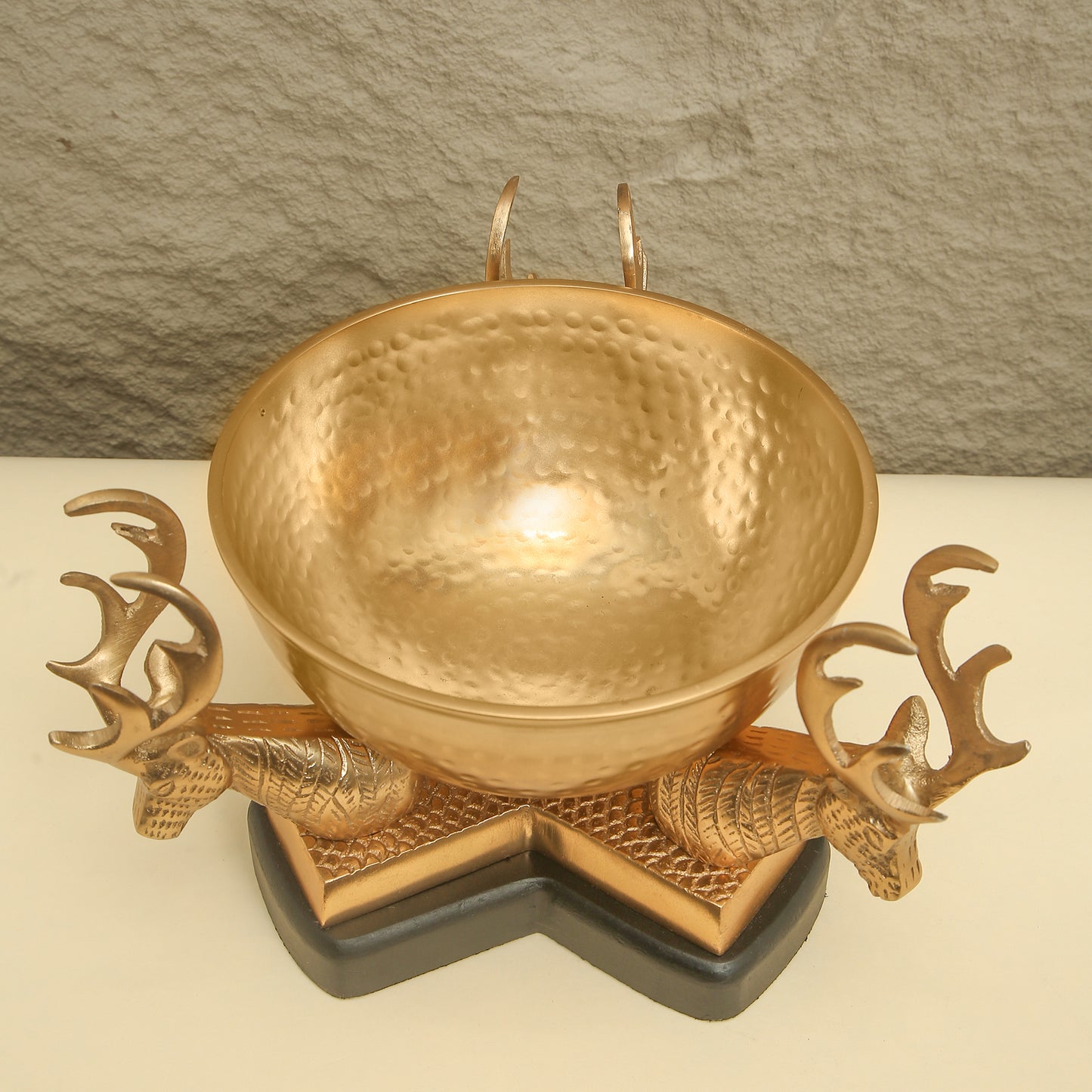 Gold bowl with deer head designs on a stone background