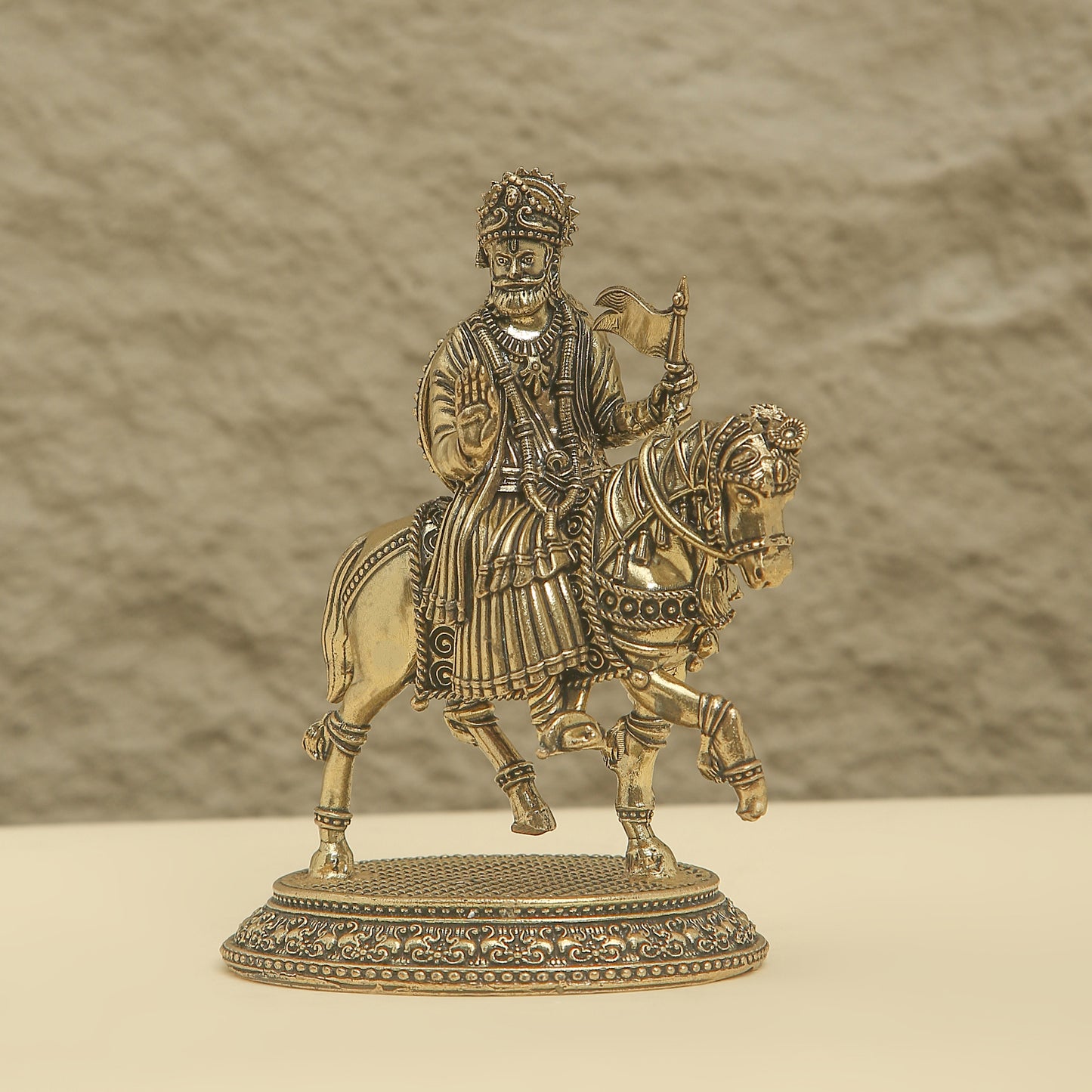 Bronze statue of a warrior on horseback with intricate details against a beige background
