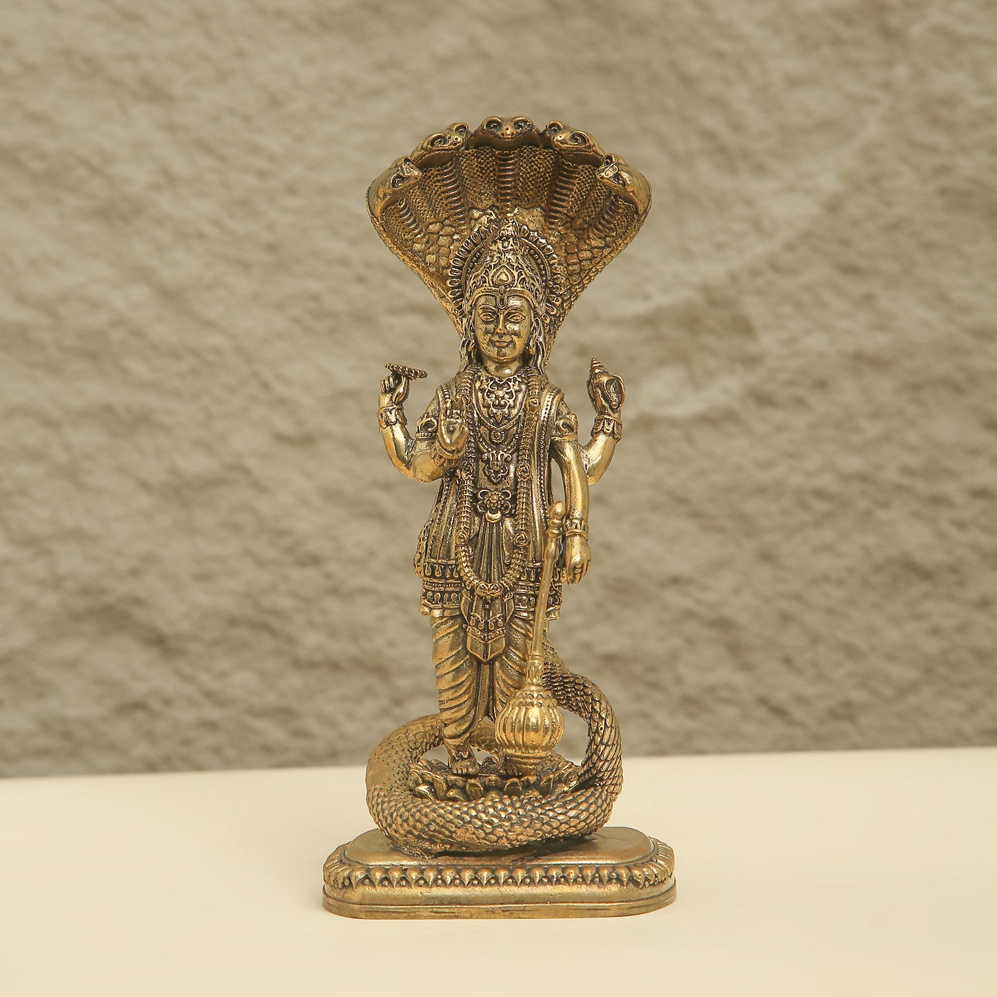 Gold-colored statue of a deity with intricate details on a textured beige background