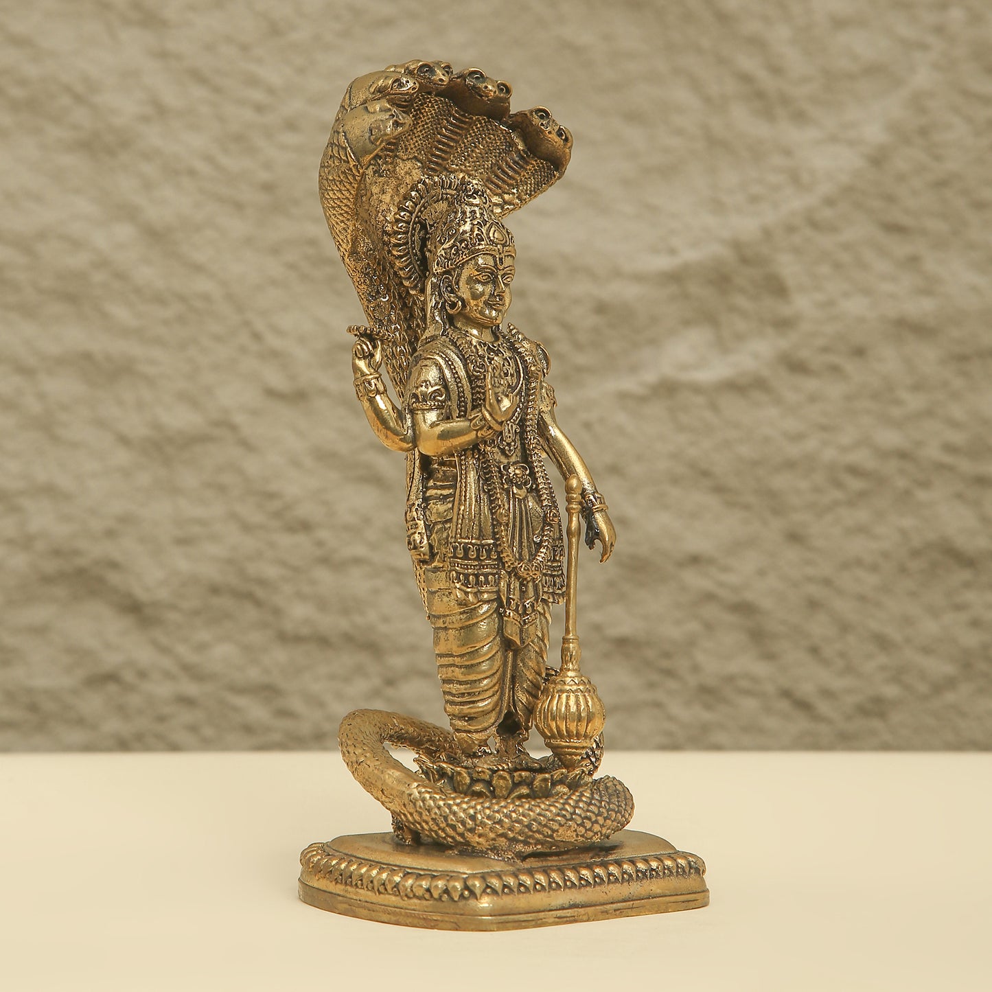 Bronze statue of a deity with a snake on a beige background
