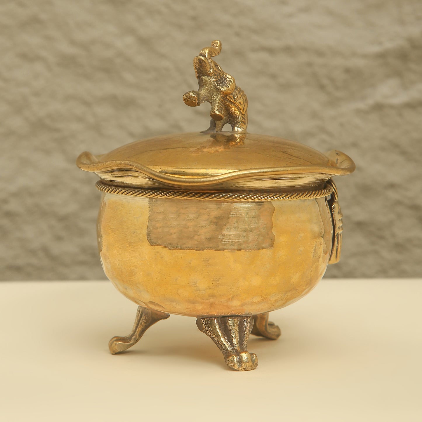 Gold-colored decorative container with a lid featuring a figurine on a beige background