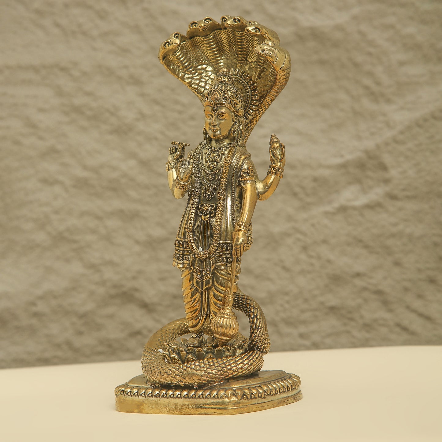 Gold-colored statue of a deity with a snake on a beige surface and brown background