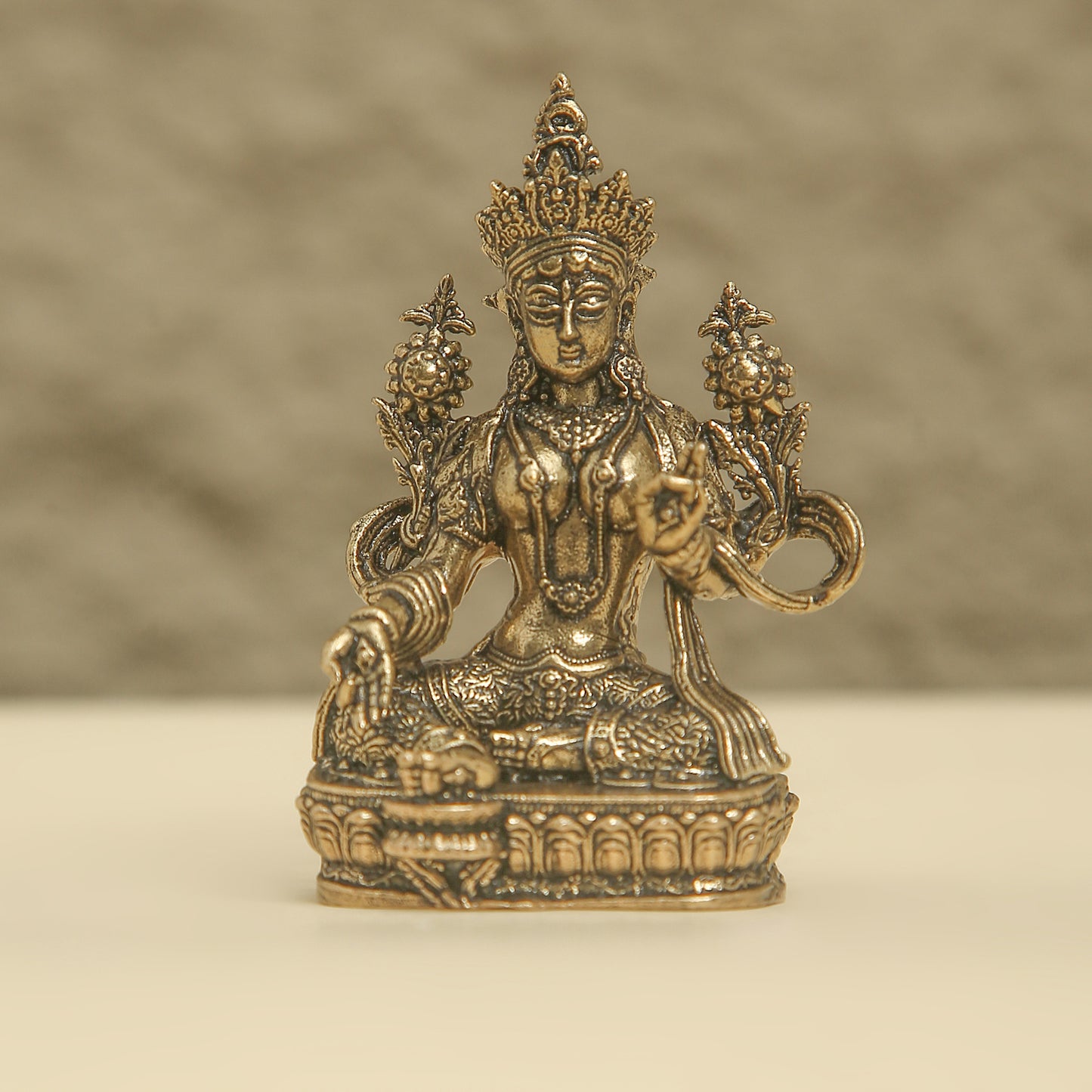 Bronze statue of a deity with intricate details on a beige background