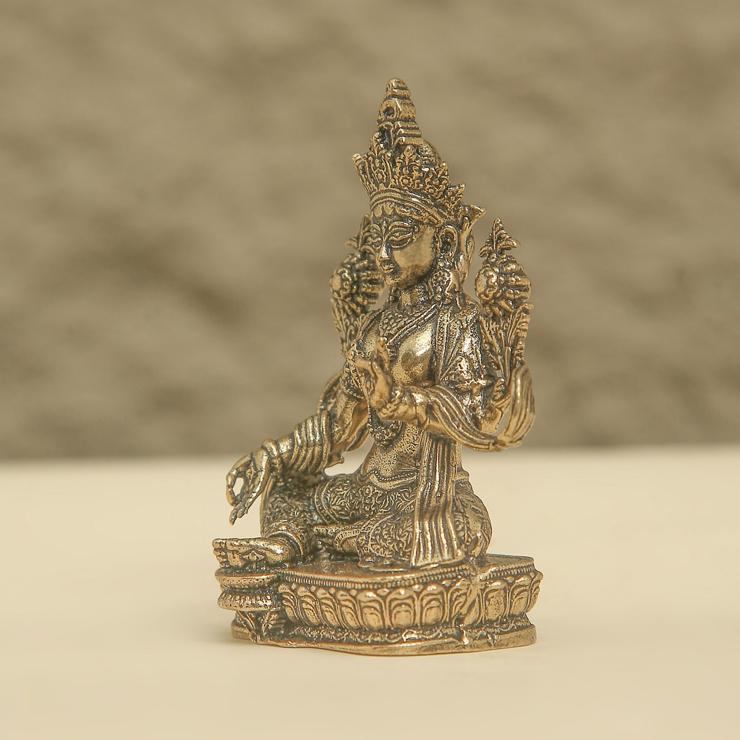 Bronze statue of a seated figure with intricate details on a beige background