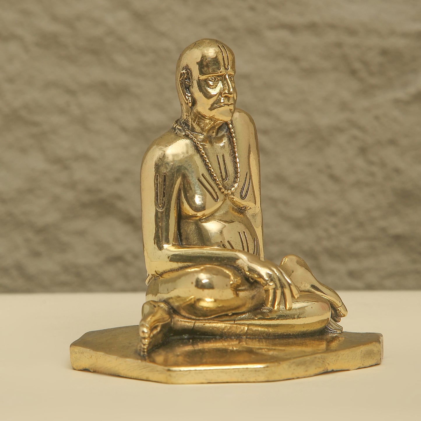 Gold statue of a seated figure on a beige surface with a neutral background