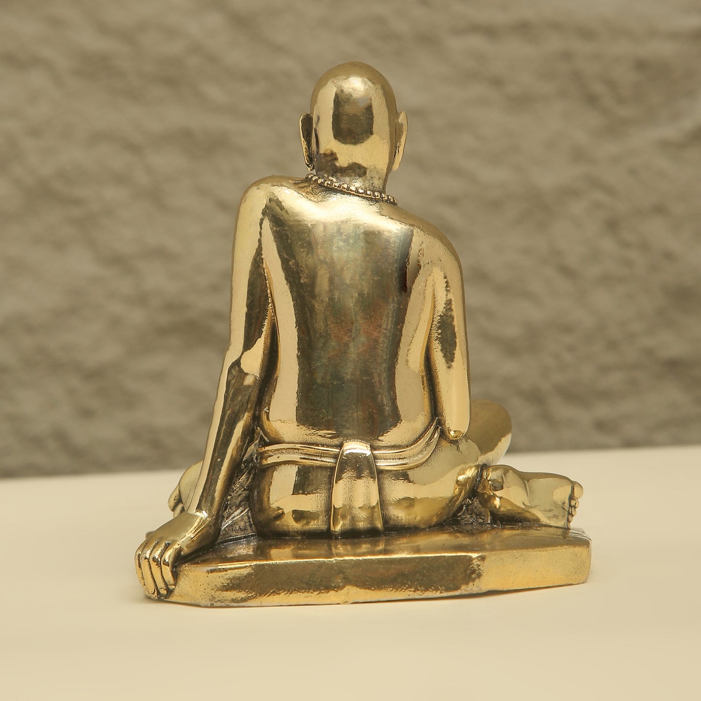 Gold-colored statue of a seated figure on a neutral background