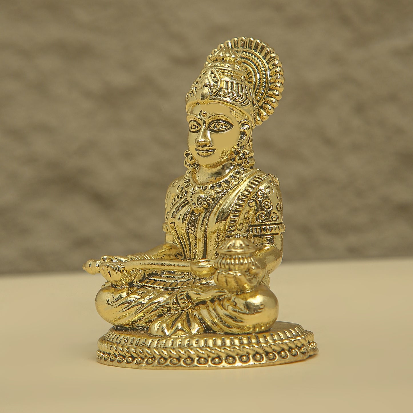 Gold-colored statue of a seated figure with intricate detailing on a beige background