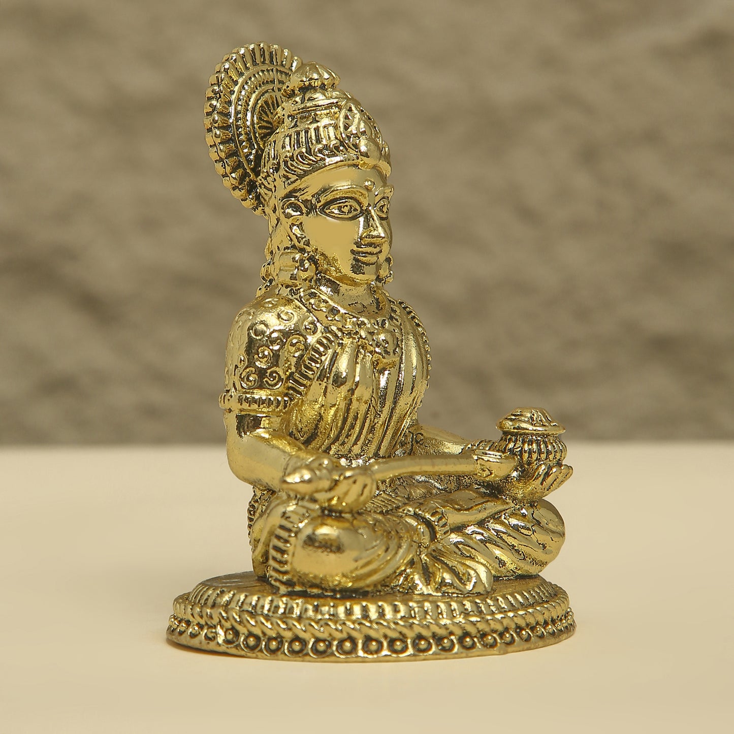 Gold-colored statue of a seated figure with intricate details on a beige background