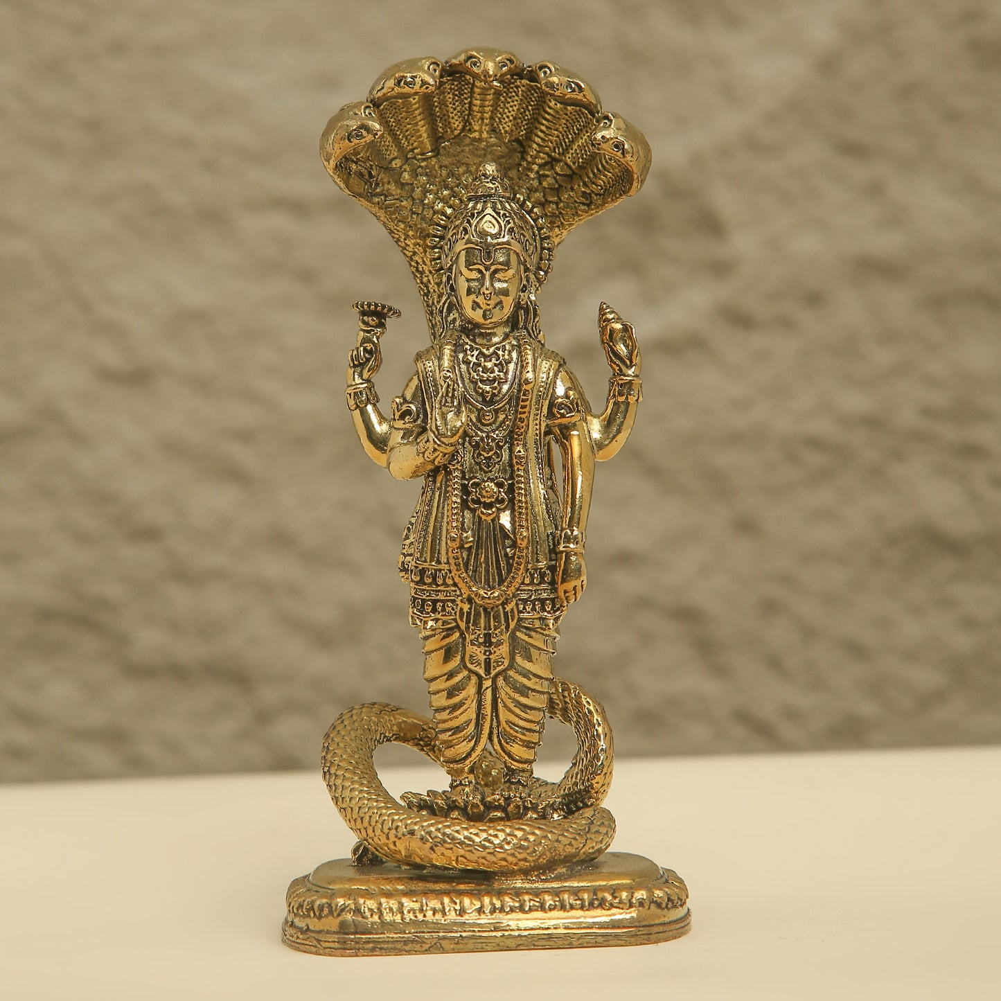 Brass statue of a deity with a snake on a beige background