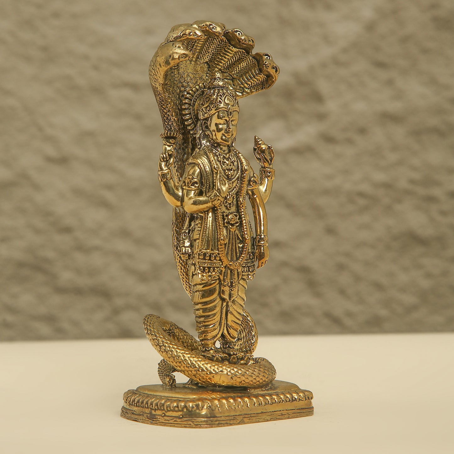 Gold-colored statue of a deity with a snake on a textured background