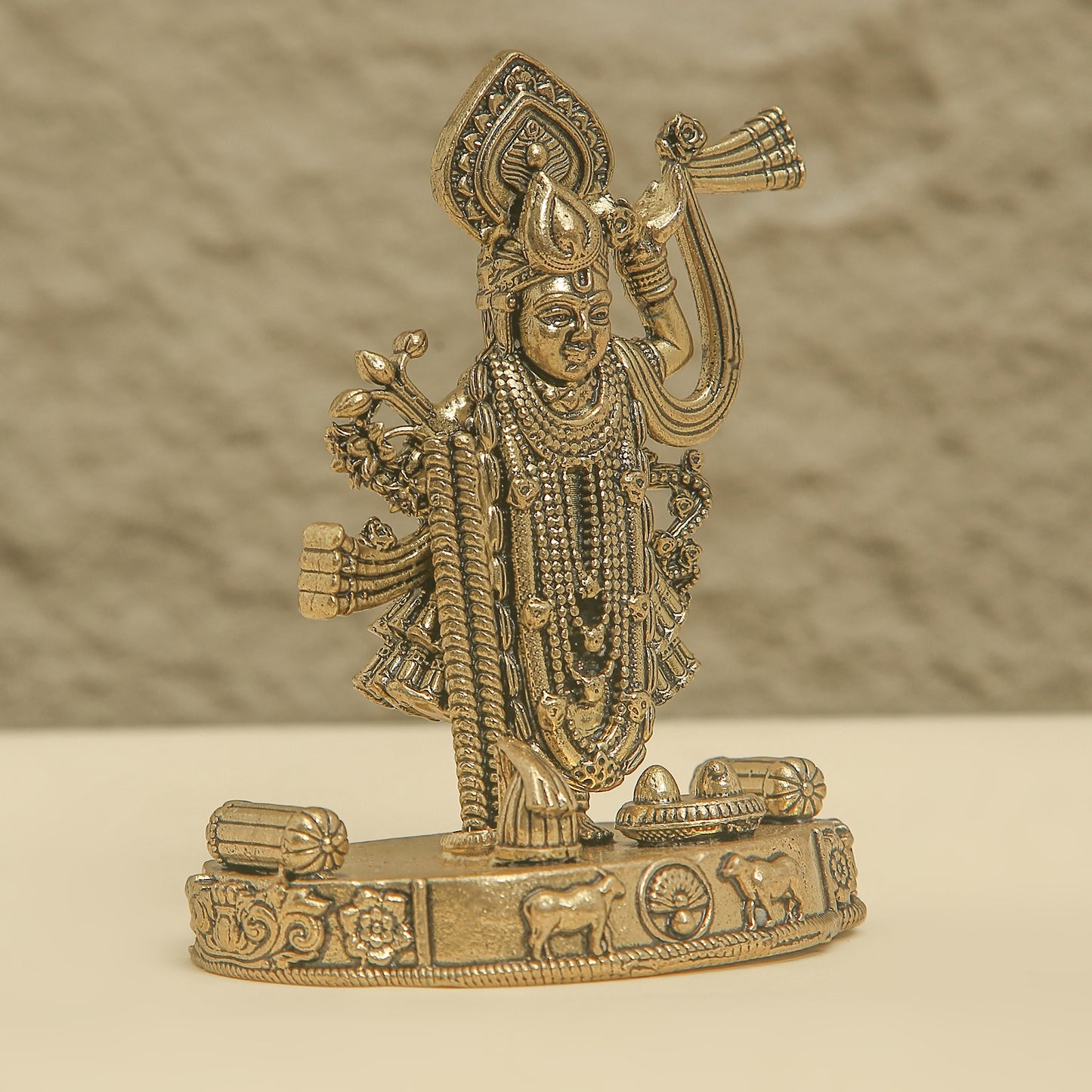 Gold-colored statue of a deity on a beige surface with a neutral background