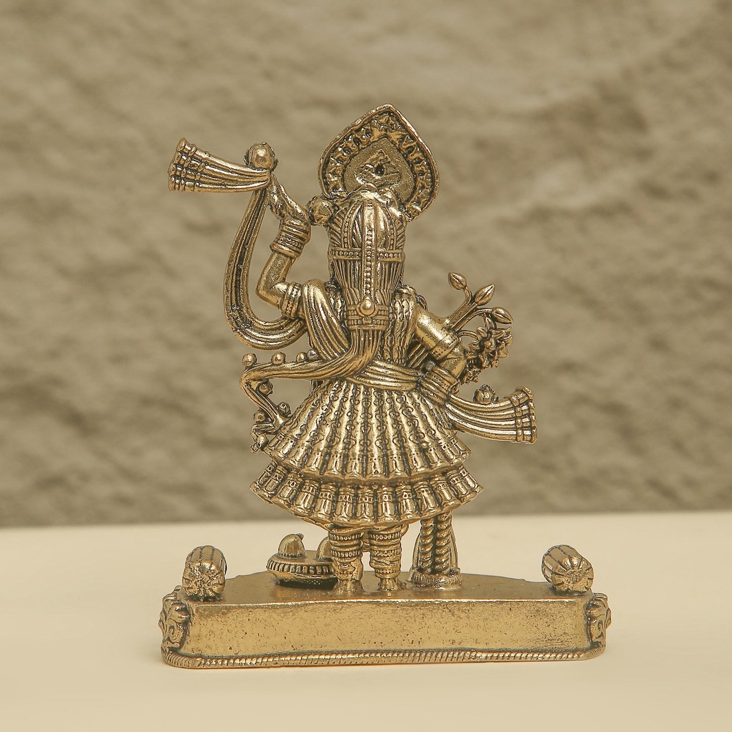 Gold-colored figurine of a deity on a textured beige background