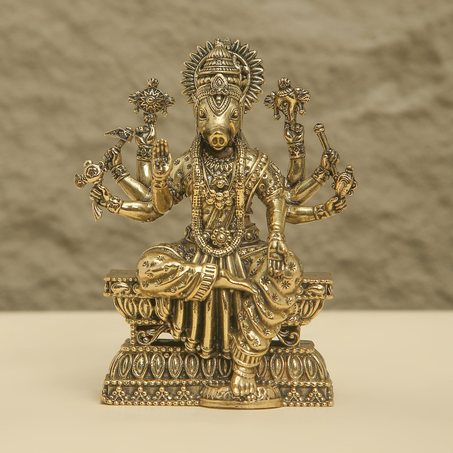 Gold-colored statue of a deity with multiple arms on a beige background
