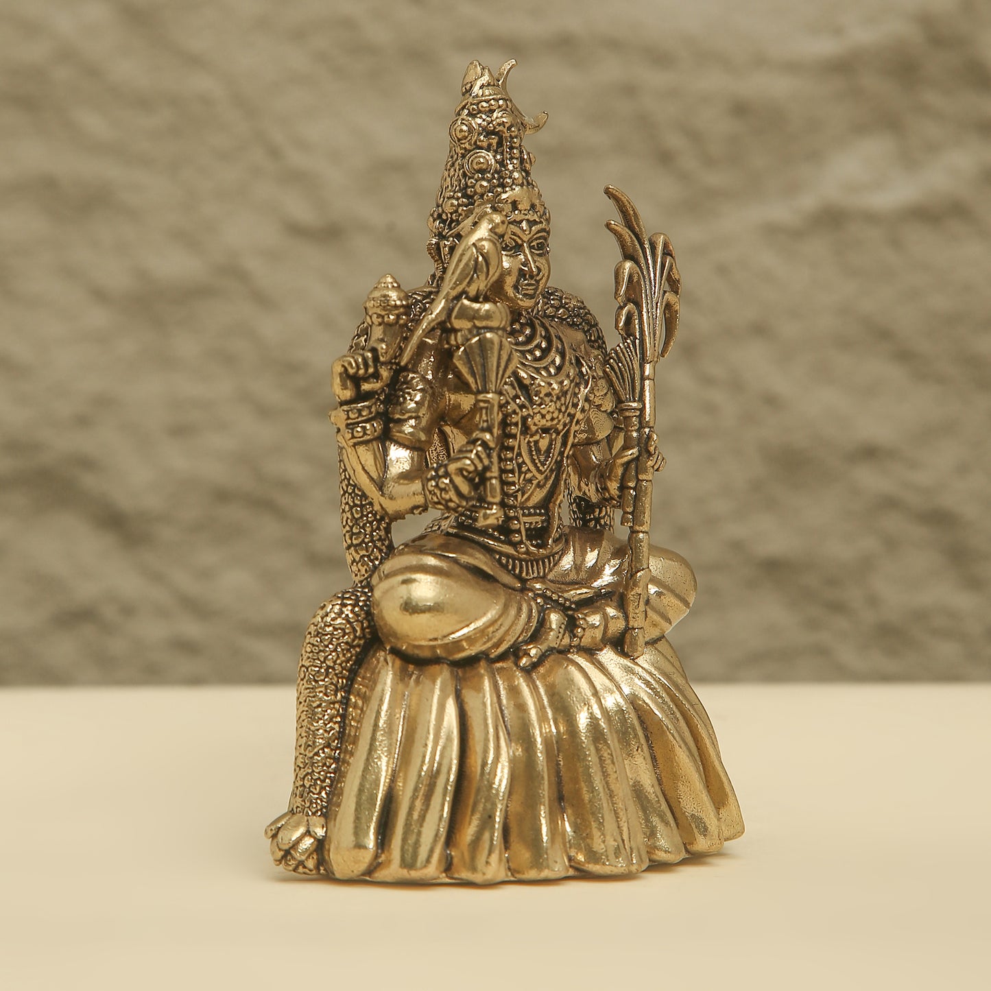 Bronze statue of a seated figure with intricate detailing on a beige surface and brown background