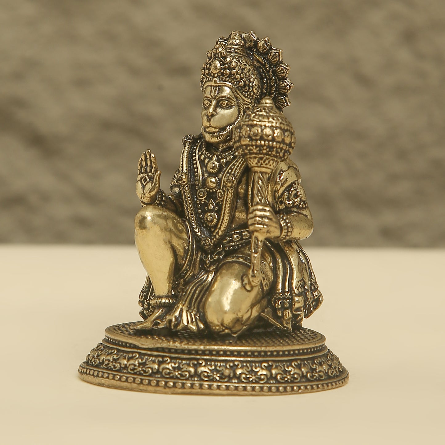 Bronze statue of a seated figure with intricate details on a beige background