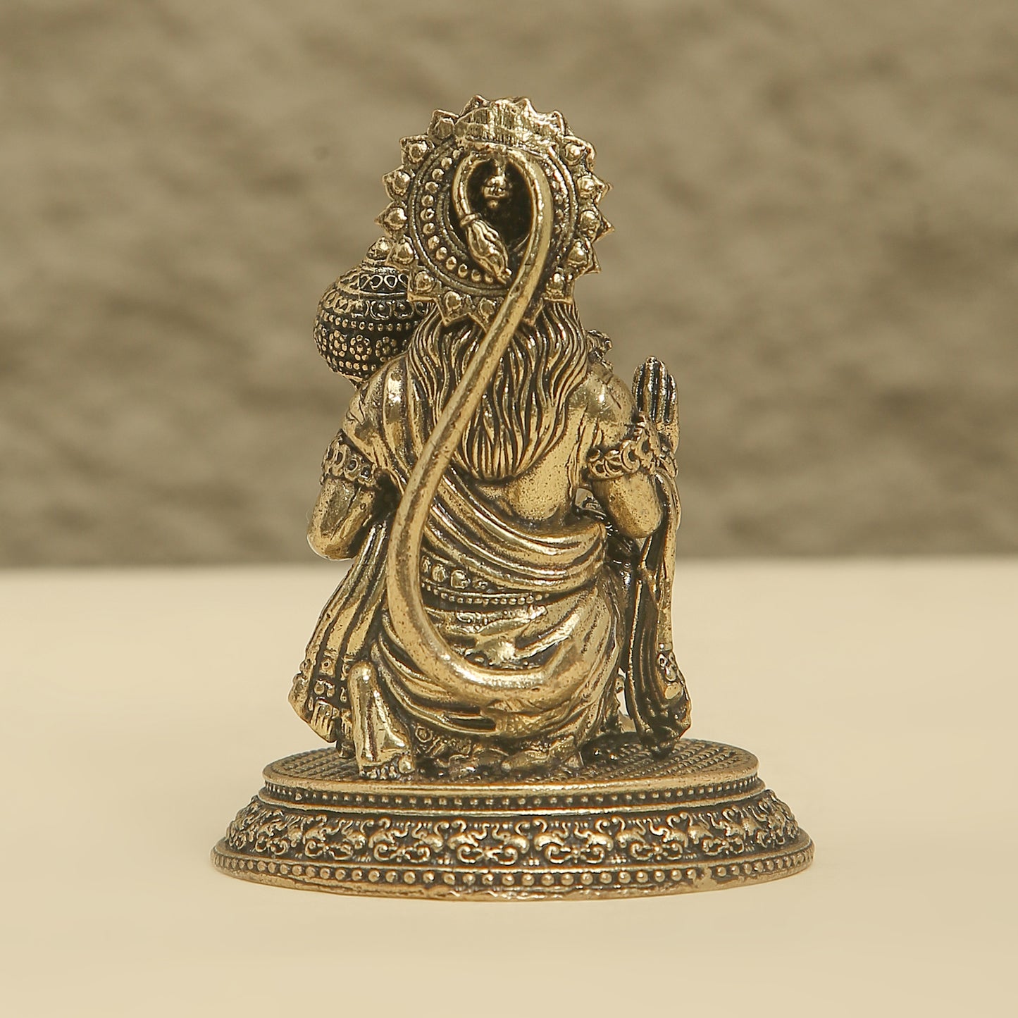 Bronze statue of a seated figure with intricate details on a beige background