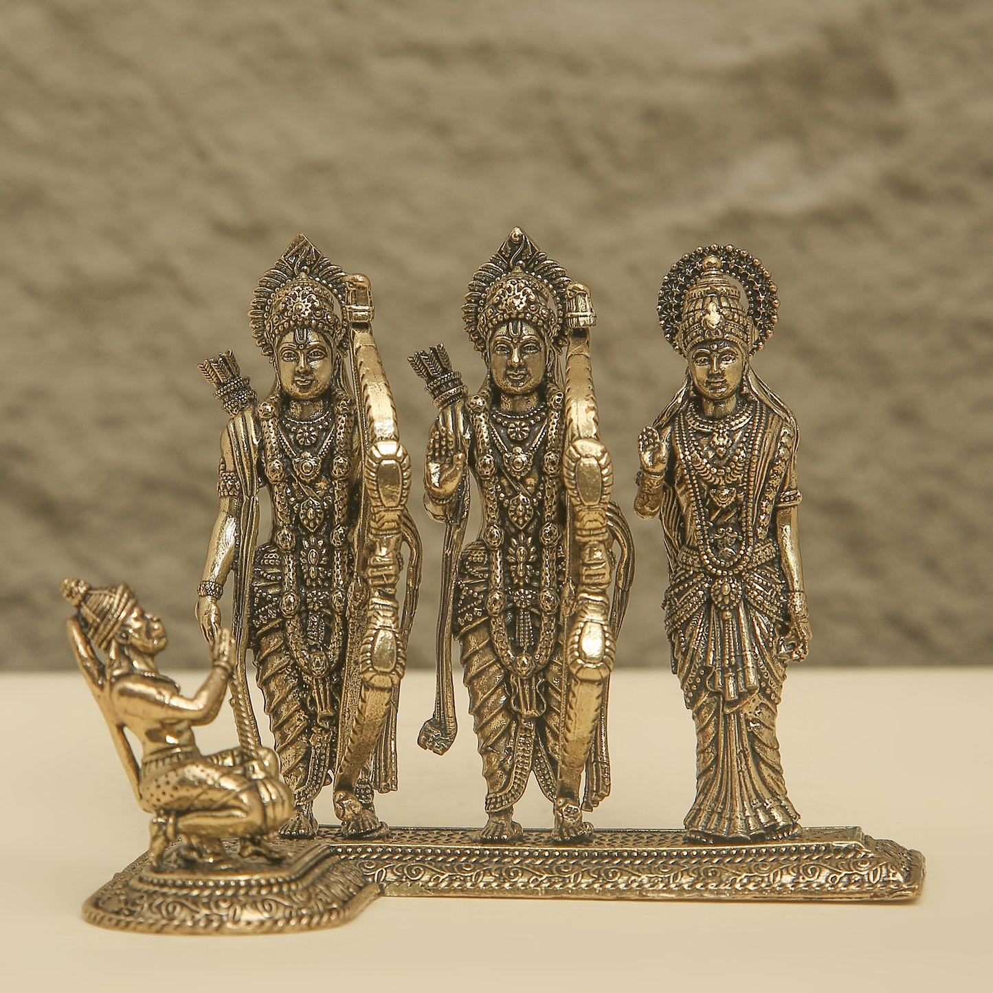 Decorative bronze figurine of three standing figures and one kneeling figure on a textured background