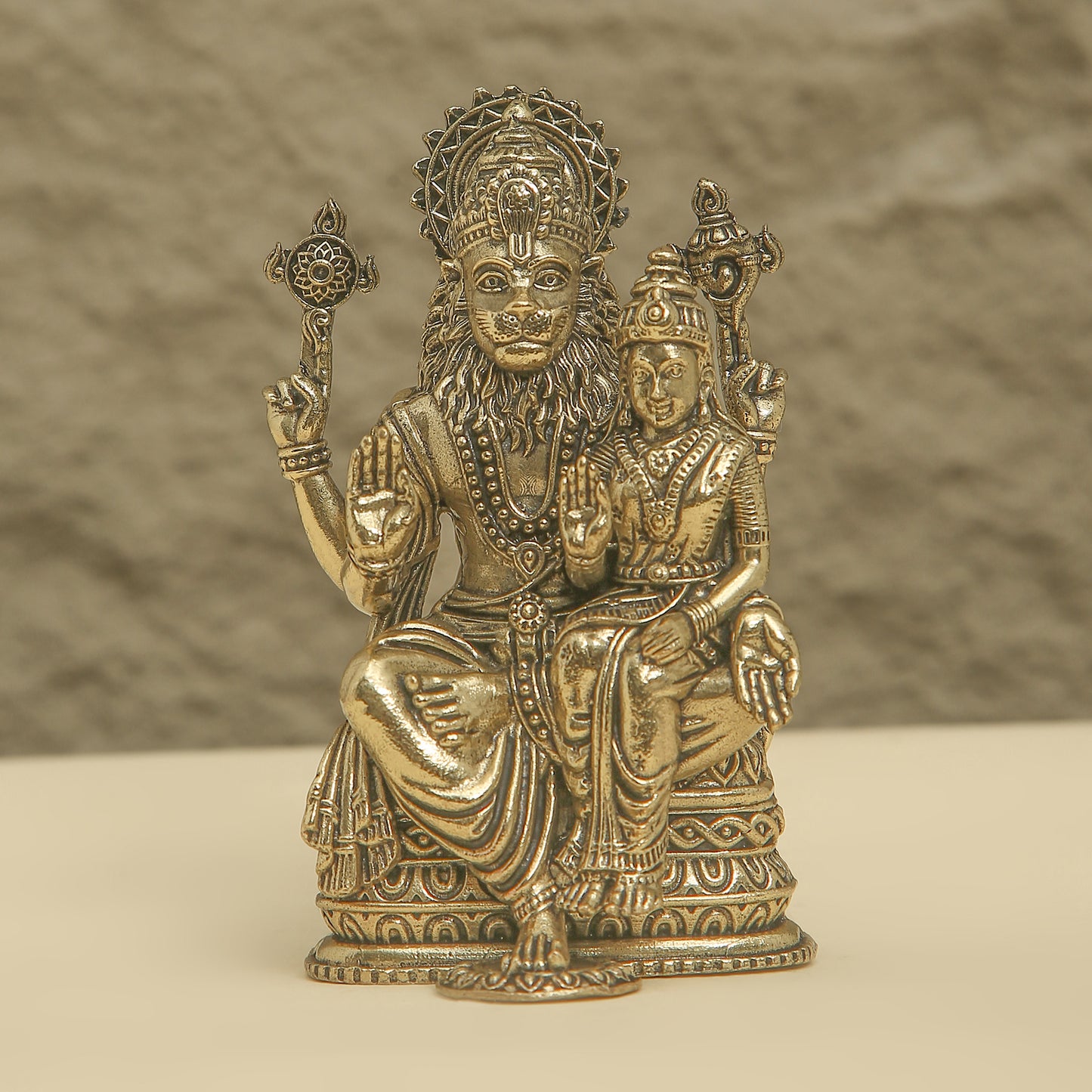 Bronze statue of a seated figure with another figure on its lap against a textured brown background