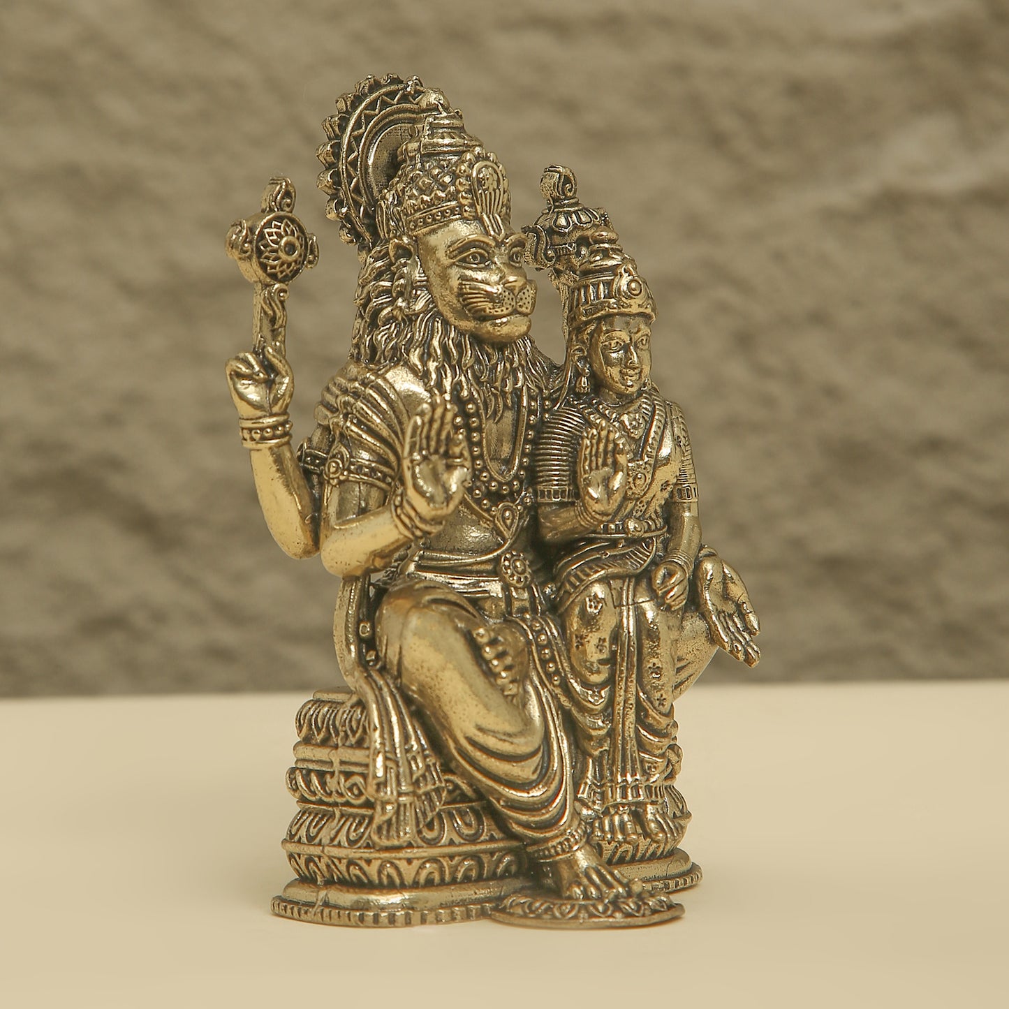 Bronze statue of a seated figure with another figure on its lap against a textured brown background