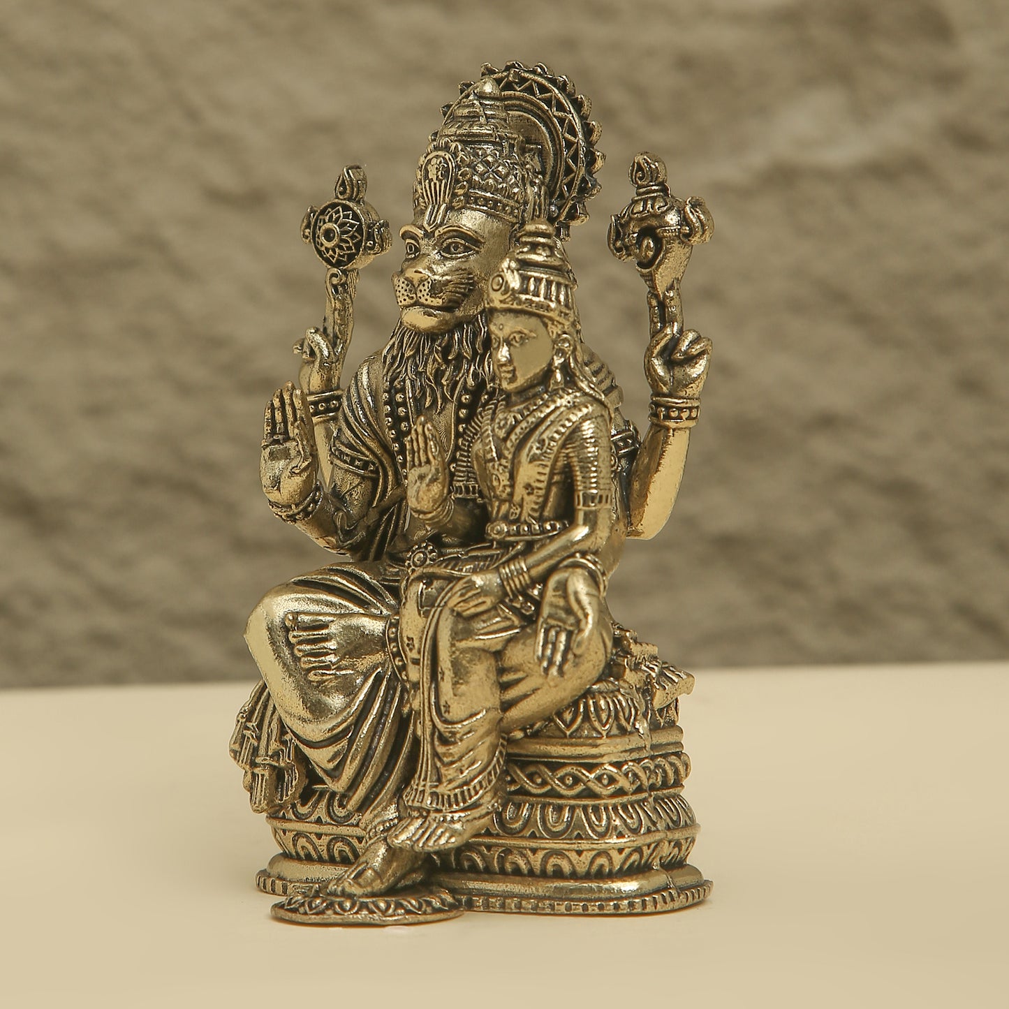 Bronze statue of a seated figure with intricate details on a beige background