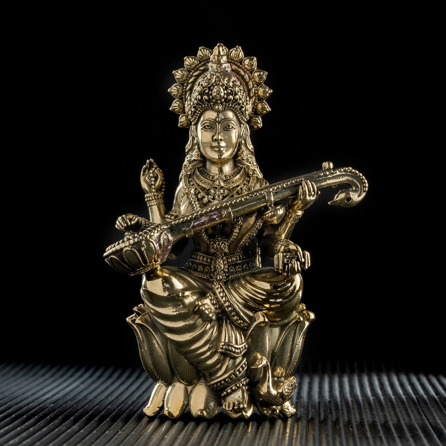 Gold-colored figurine of a seated figure playing a stringed instrument on a textured surface with a black background
