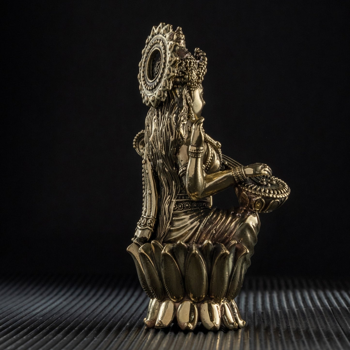 Bronze sculpture of a figure with a crown on a textured surface with a black background